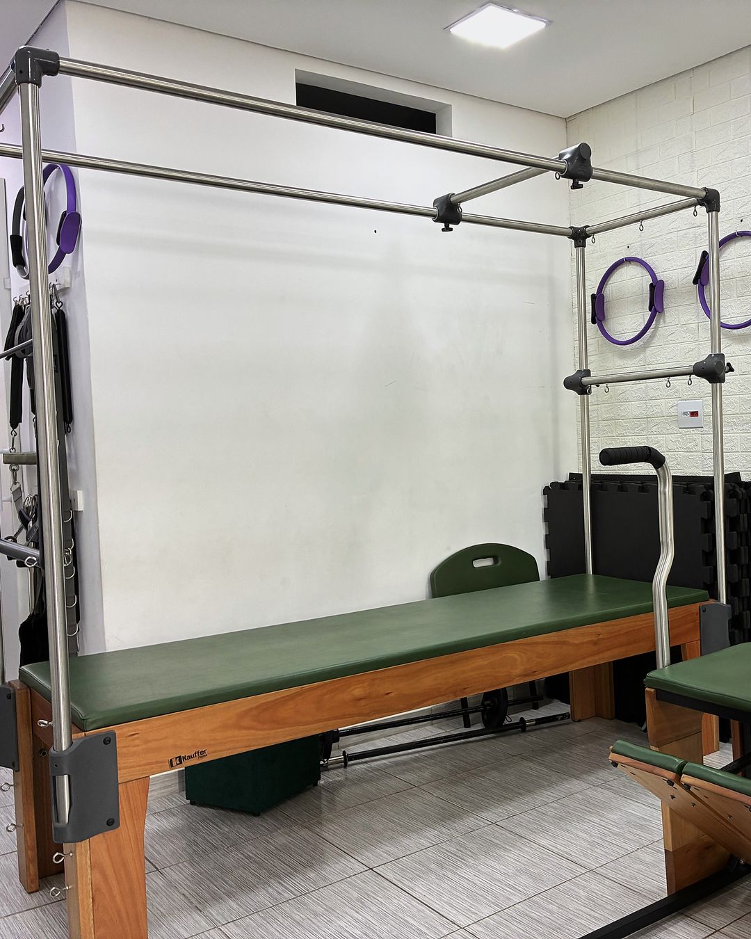 A sala de Pilates do estúdio: cadillac com barras e molas, cadeira ao lado e arcos na parede.